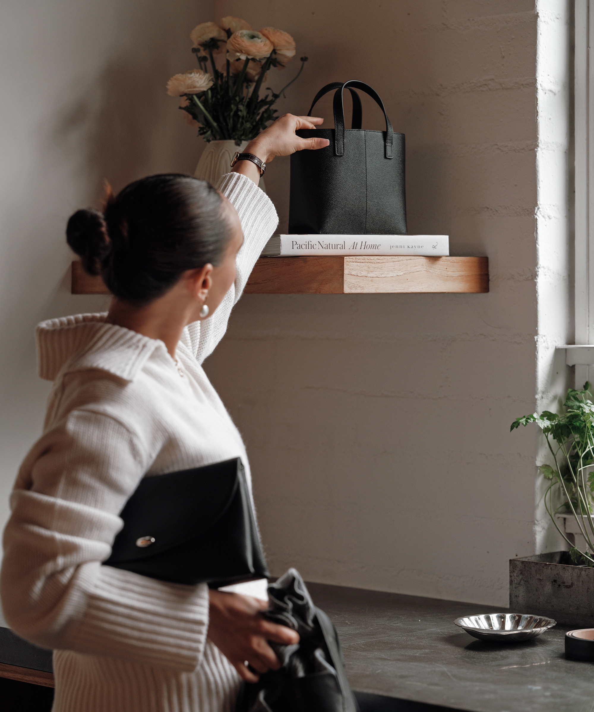 julia wearing an ivory sweater placing a purse on a shelf in a kitchen