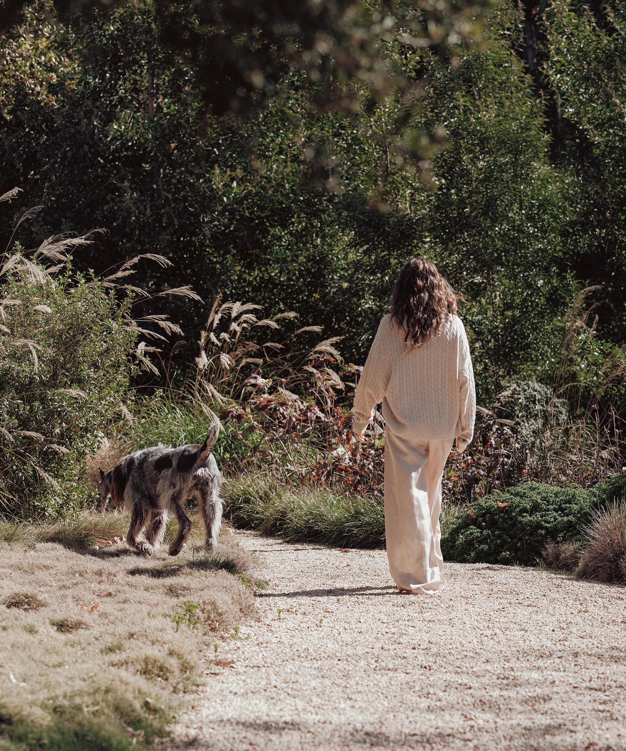 jenni walking on a gravel path wearing the alabaster nell sweater with her dog