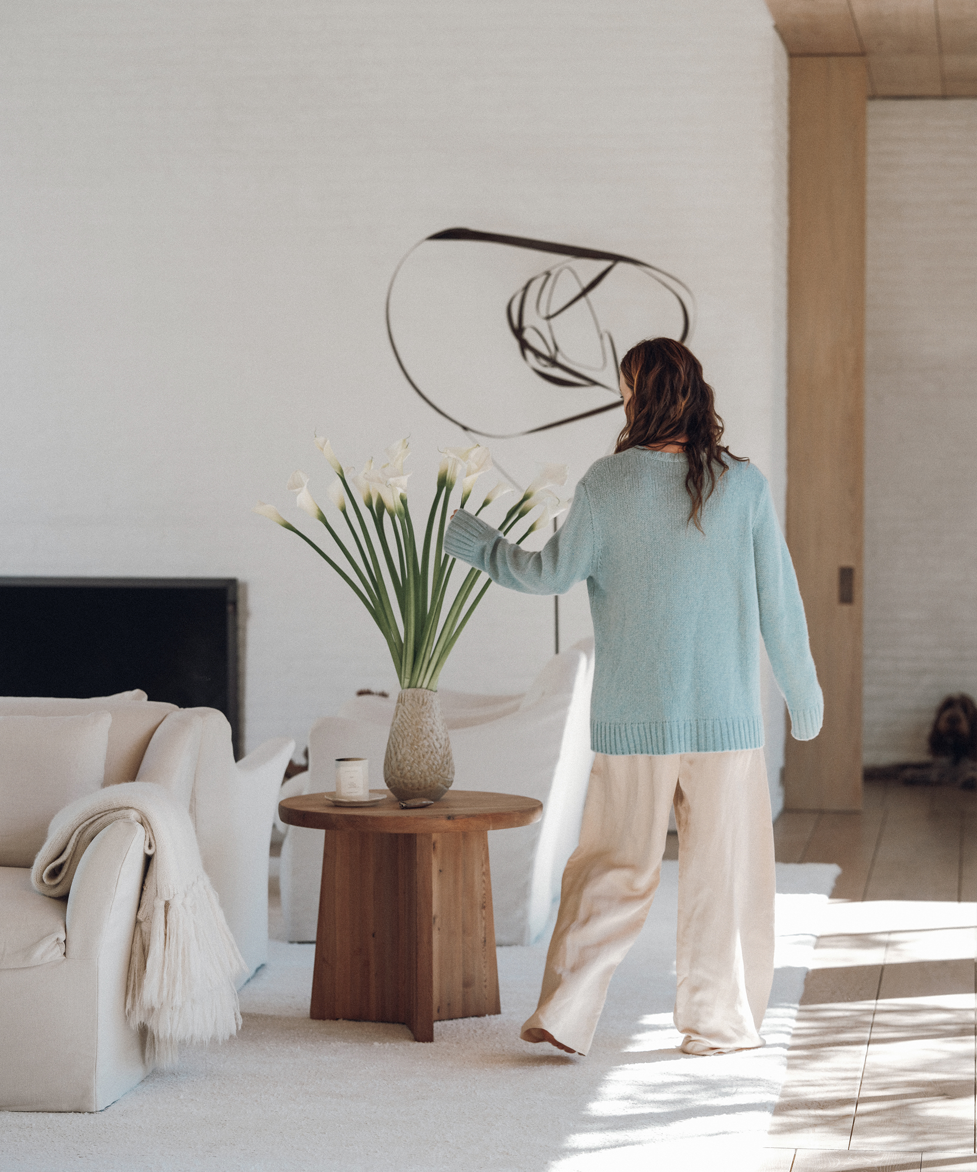 jenni wearing a blue cashmere sweater and oatmeal linen pants walking in a living room with an ivory rug