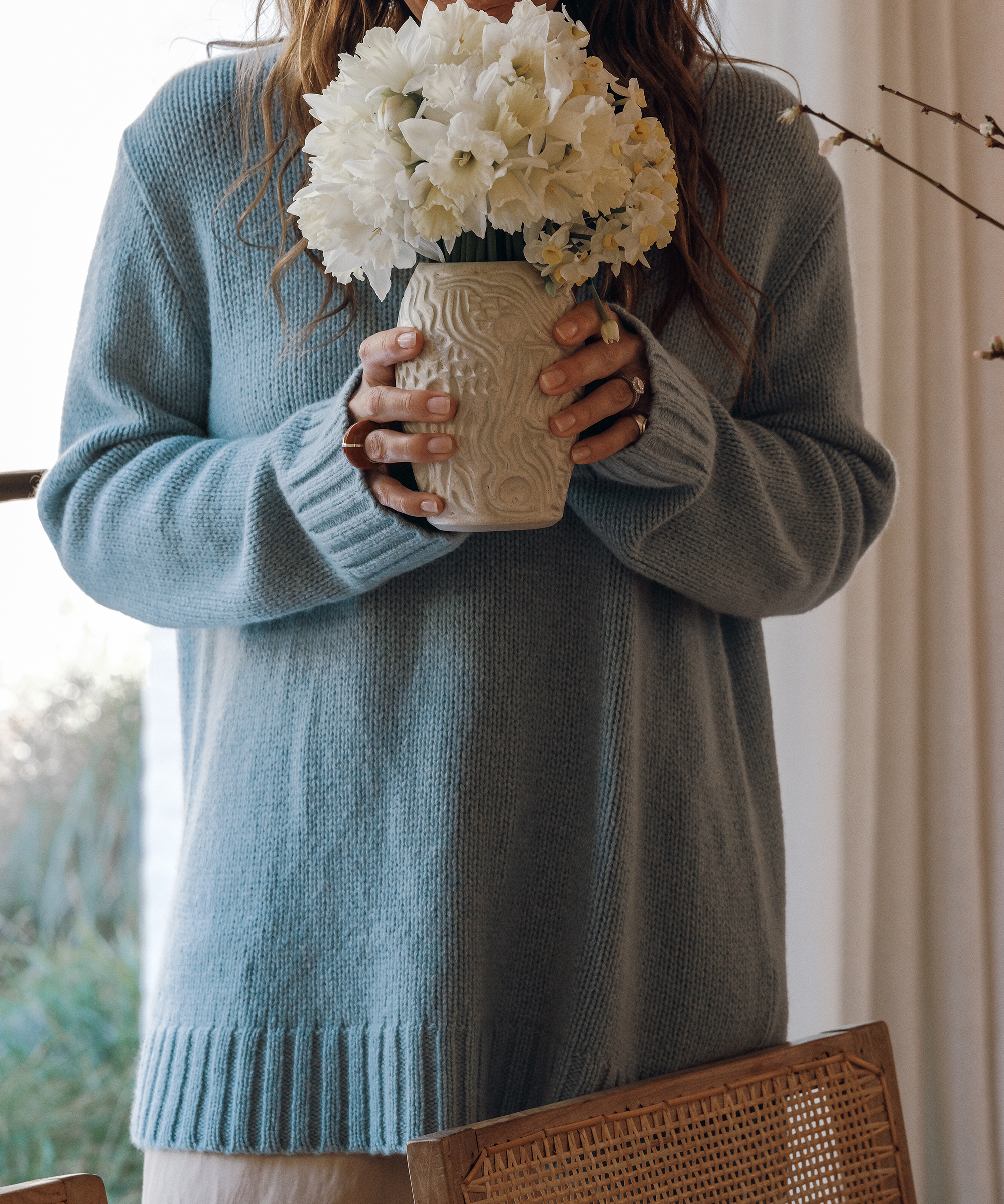 jenni wearing a blue sweater holding an ivory vase with white florals