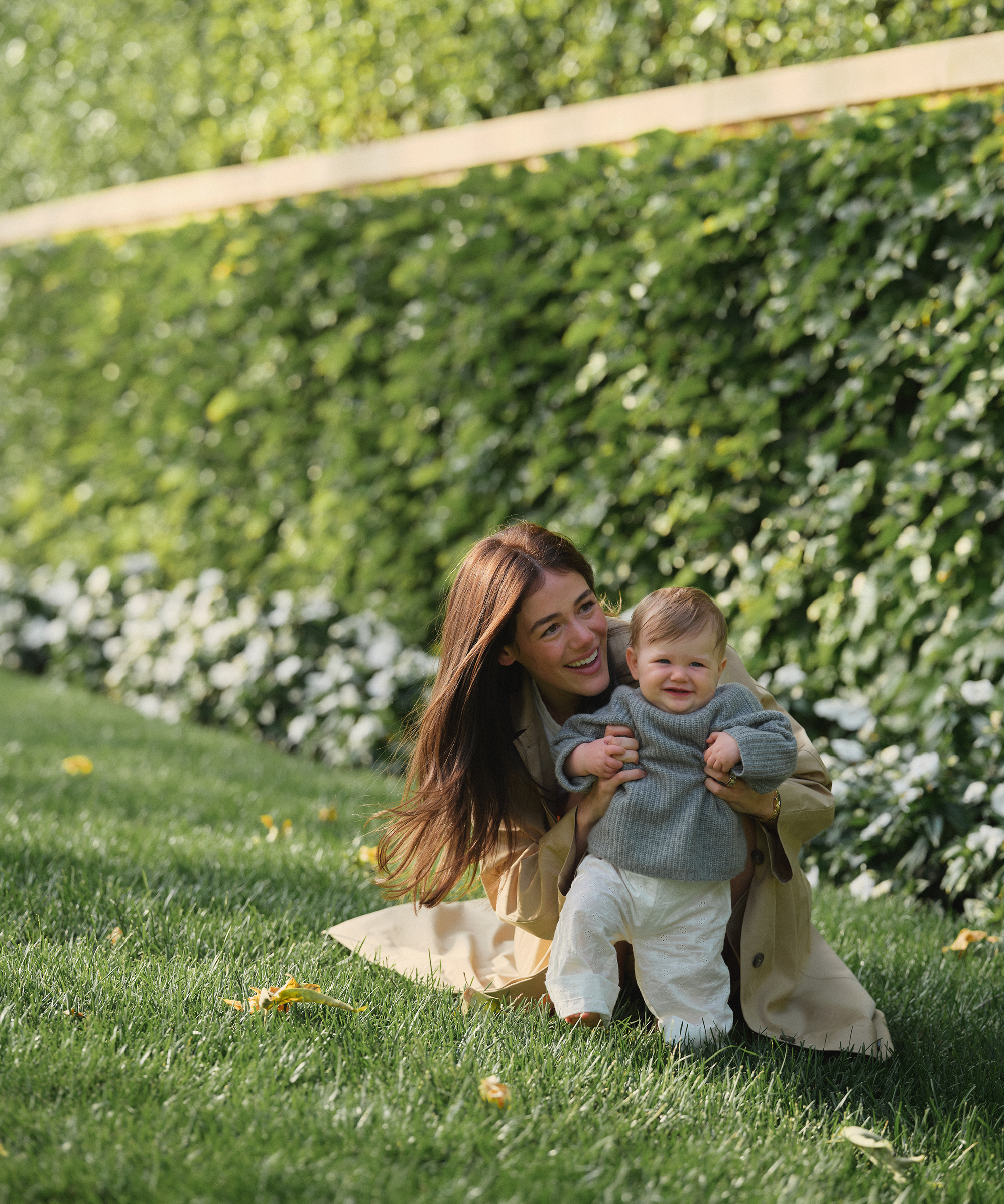 ilana wearing a trench outside holding her baby in a cashmere fisherman