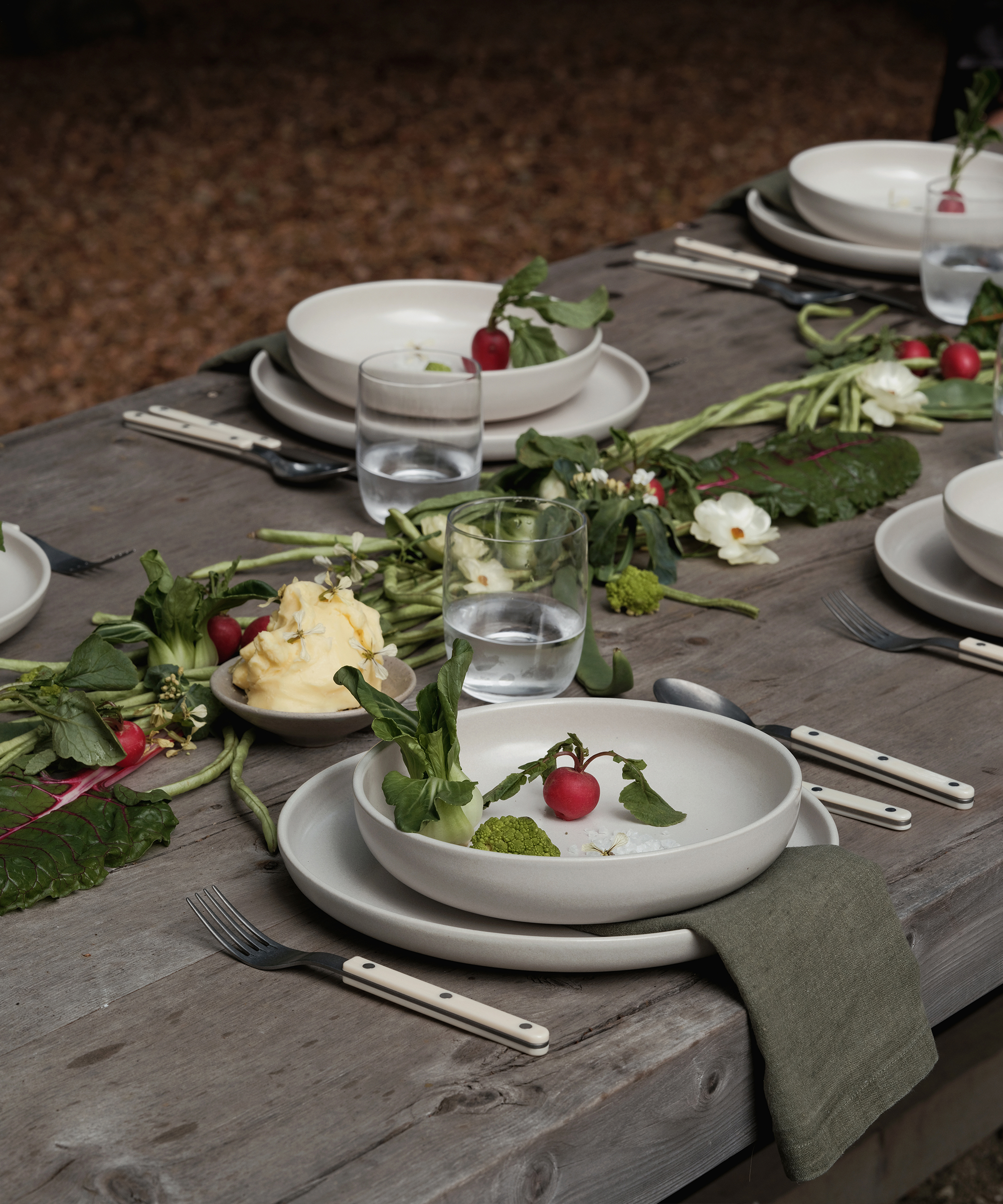 a table with ivory dinner plates with radishes and a green linen napkin and ivory cutlery