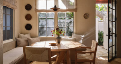 a dining room with light shining in and a wooden round table and wooden dining chairs