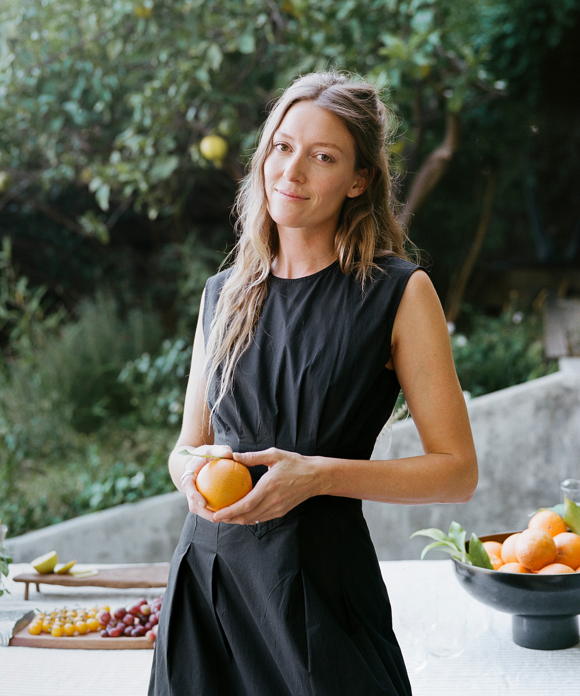 a woman in a black dress standing in front of a table holding an orange