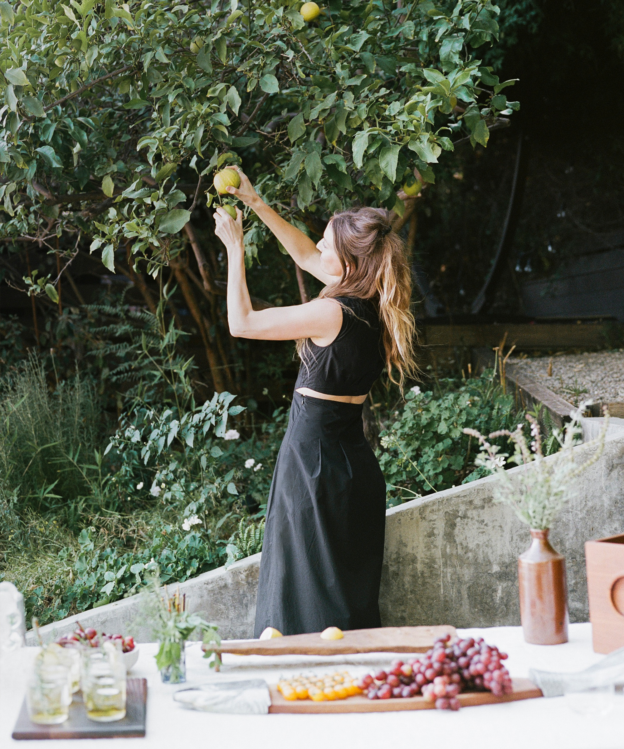 a woman in a black dress picking lemons off a tree in her backyard