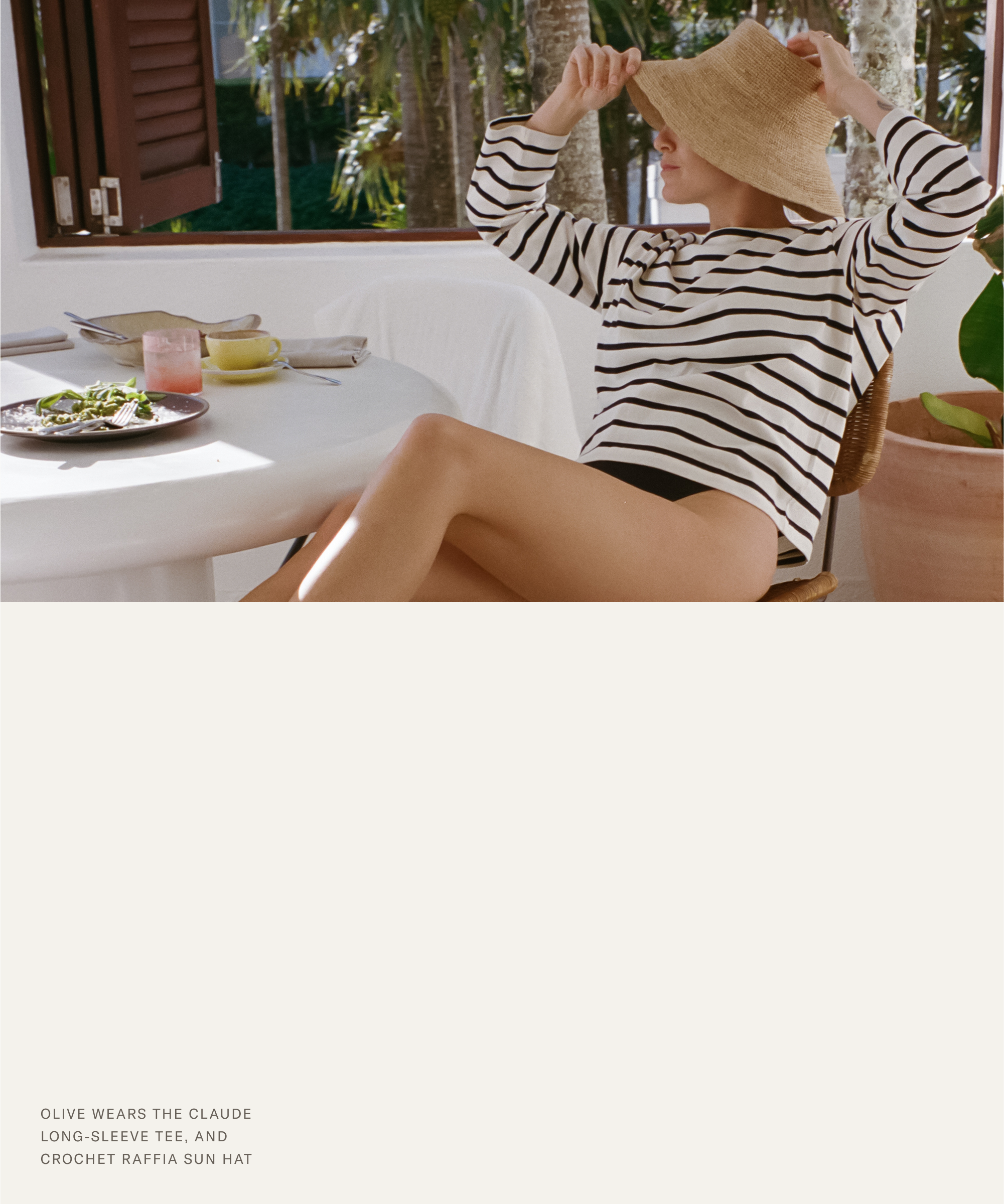 Olive Cooke sits at an outdoor table in a striped long-sleeve shirt and black shorts, adjusting her wide-brimmed raffia sun hat. Sunlight filters through tropical plants as she enjoys a partially eaten meal nearby.
