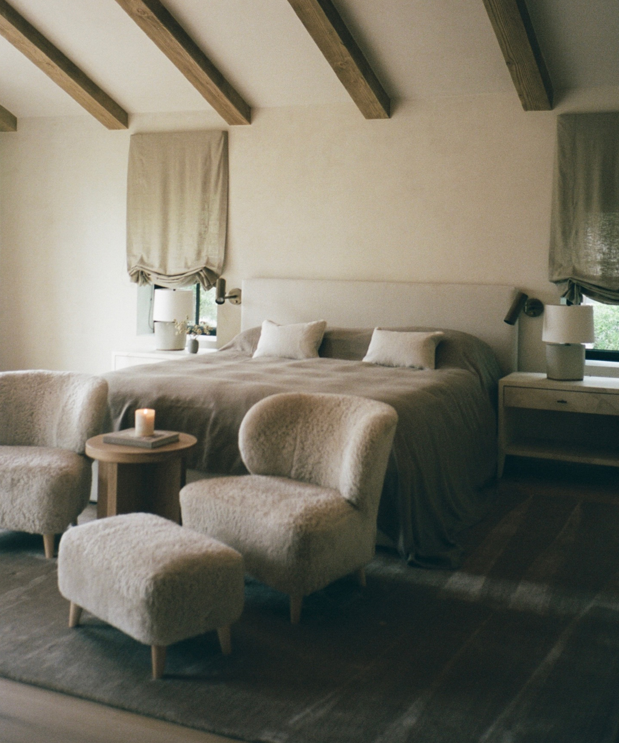 a primary bedroom with a taupe headboard and shearling accent chairs with vaulted ceilings