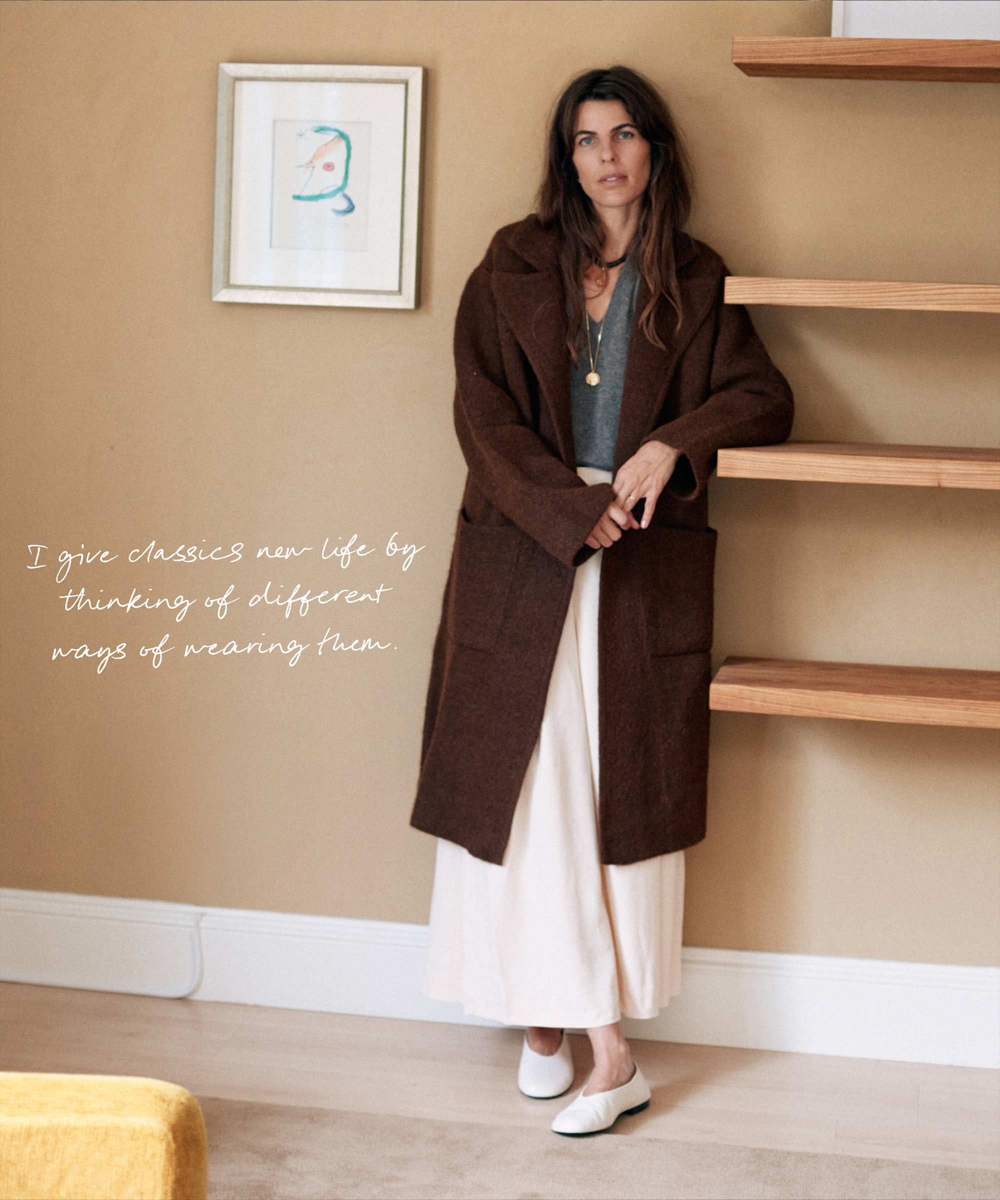 A woman, inspired by Laura Vidrequin Roso, stands indoors in a long brown coat over a white skirt and flats. In a neutral-toned room, she says: “I give classics new life by thinking of different ways of wearing them.”.