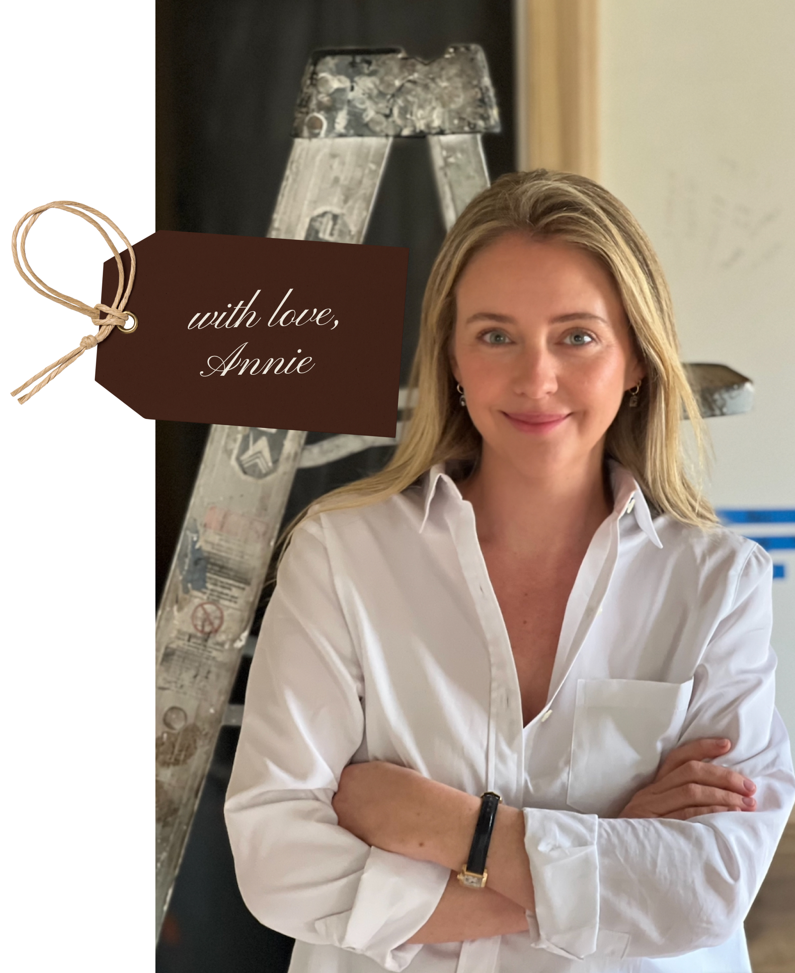 A woman with long blonde hair, wearing a white button-down shirt, stands smiling with arms crossed in front of a paint-splattered ladder. A brown tag reads "with love, Annie"—a personal touch from this oak house.