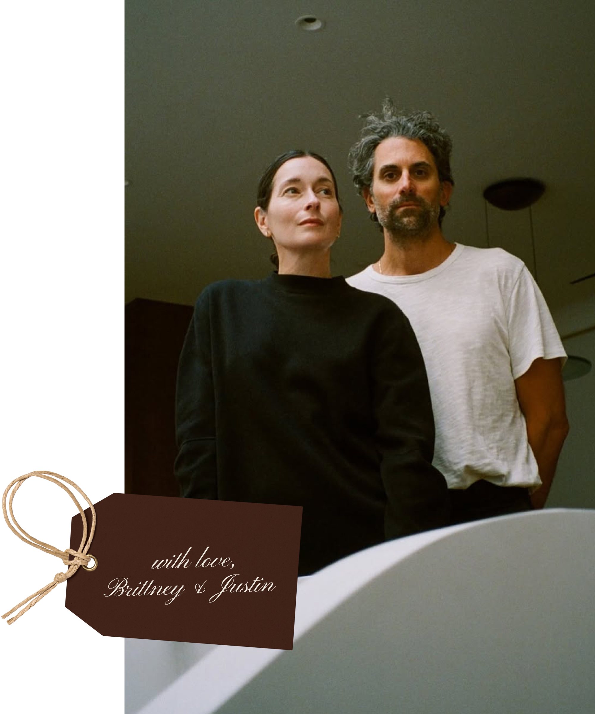 A woman in a black sweater and a man in a white t-shirt stand indoors. A brown gift tag with a string at the bottom left corner reads, with love, Brittney & Justin.