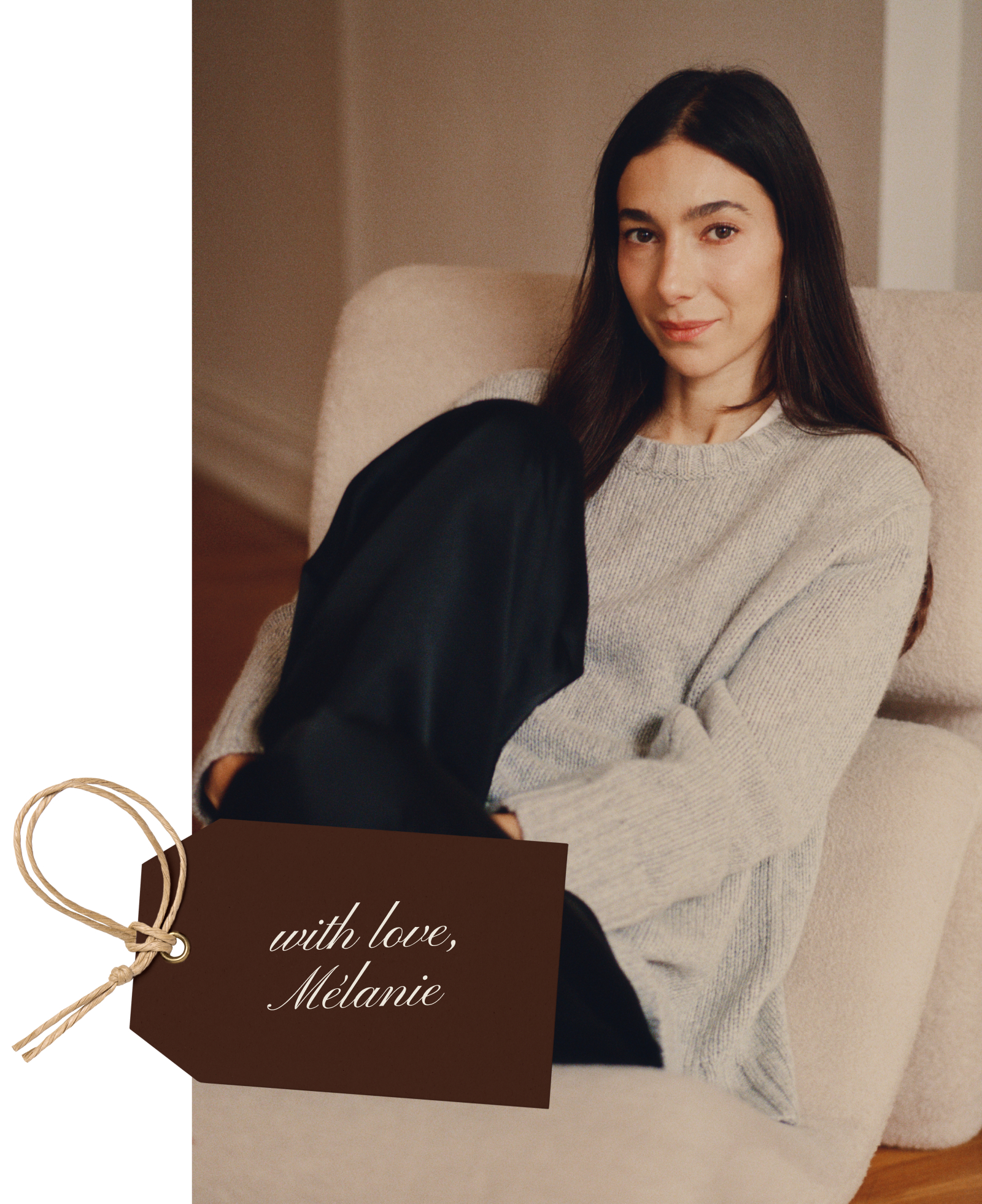 A woman with long dark hair sits on a beige armchair, wearing a light gray sweater and black pants, smiling softly. A brown tag in the corner reads with love, Mélanie in cursive.