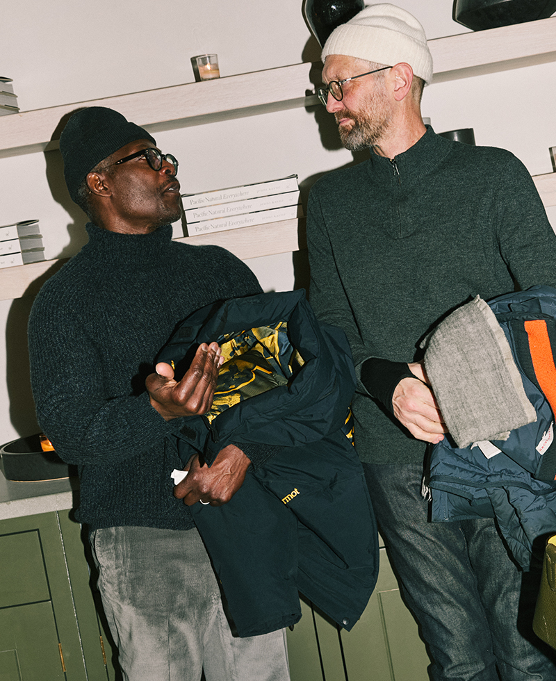 two men standing chatting leaning against a green kitchen shelf